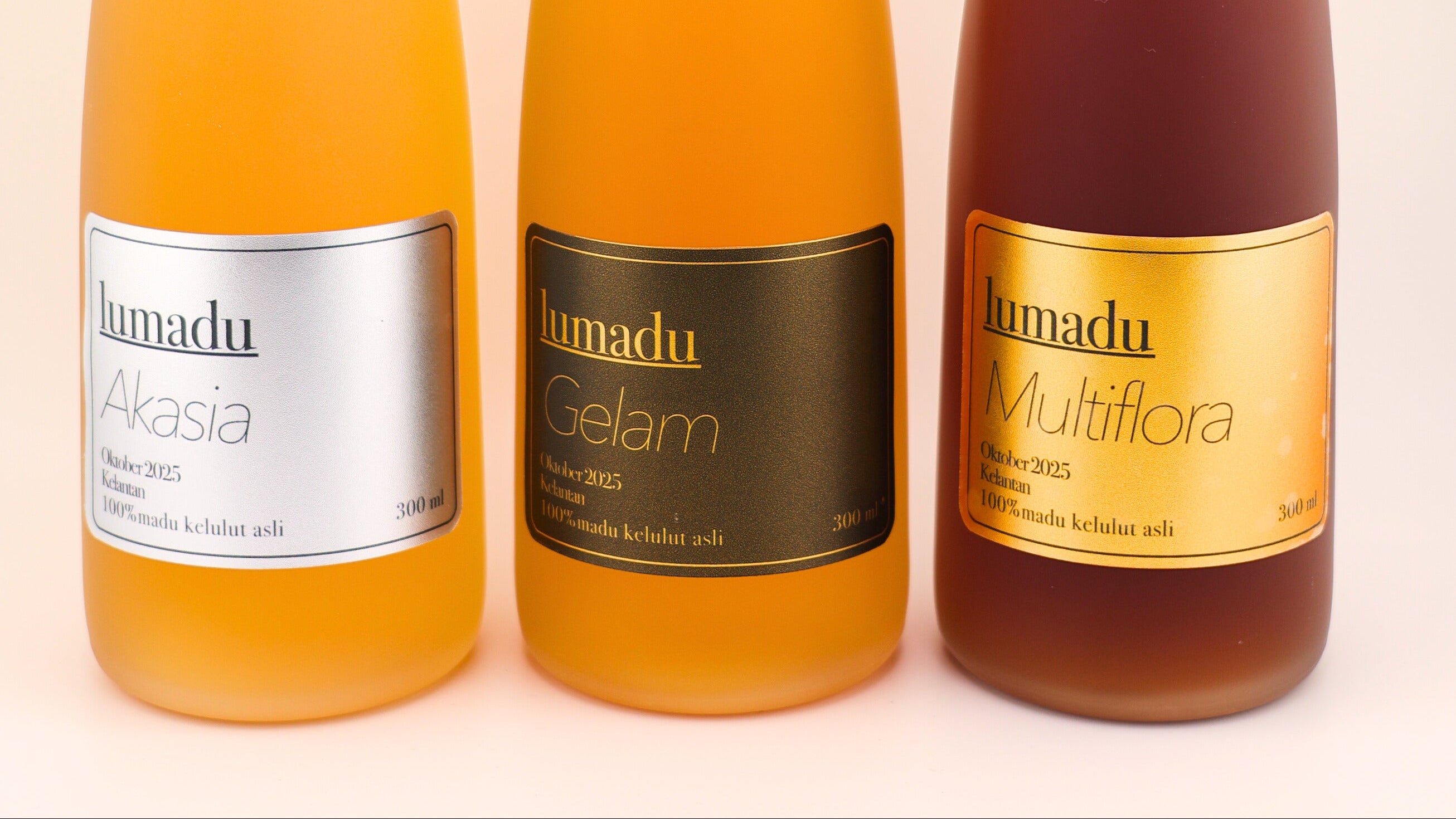 Three bottles of Lumadu Madu Kelulut with different flavors on a white background